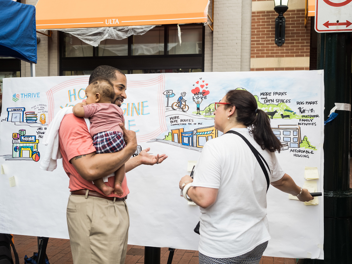 Montgomery County Councilman Will Jawando holding baby and speaking with graphic recording artist