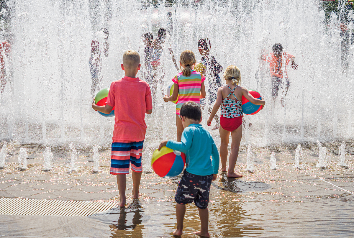 Children with beachballs playing in fountain