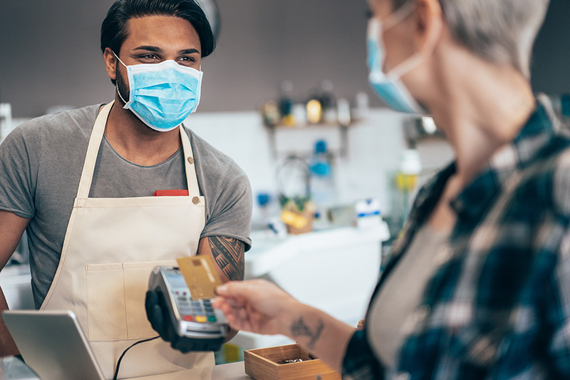 Young barista and Modern woman paying contactless at cafe wearing face protective mask to prevent Coronavirus and other diseases