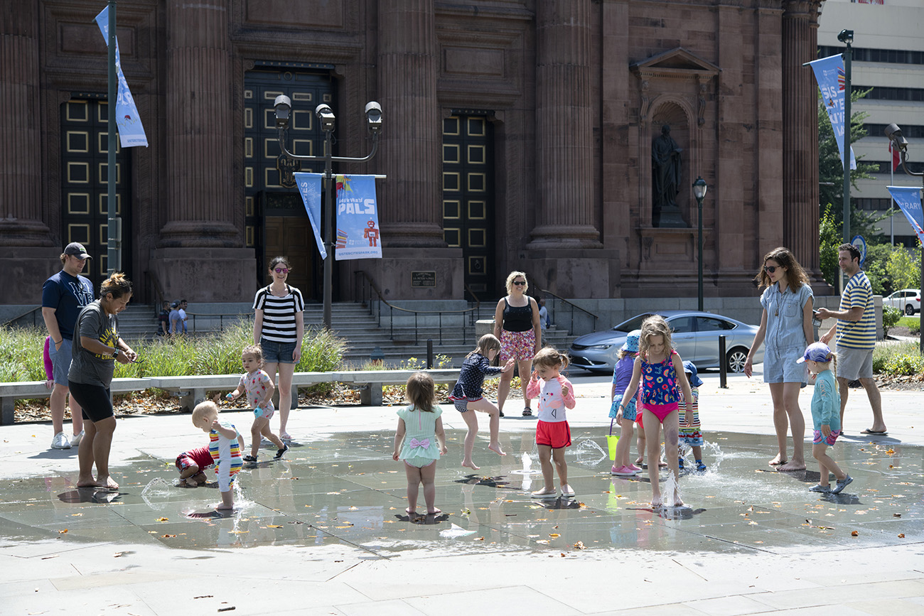 Philadelphia, USA - June 30, 2019. Children playing with small water fountains with their parents watching in front of Cathedral Basilica of Saints Peter and Paul in downtown Philadelphia, Pennsylvania.