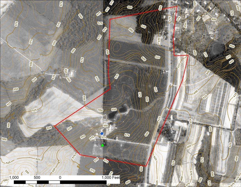 Black and white aerial photograph with historic farm boundary shown as a red line, topographic lines in yellow, a blue dot for the location of the original family house, and a green triangle in an area of trees south of the house indicating a possible location for the burial ground. A scale bar shows distance indicating that the possible cemetery location is less than 500 feet from the house.