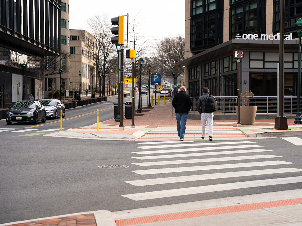 people walk in wide zebra crosswalk at intersection with traffic signals 