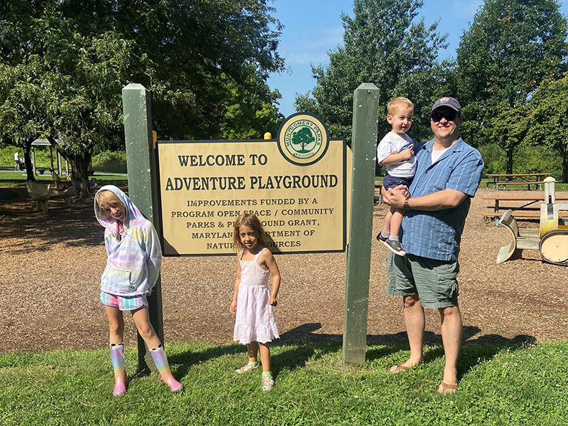 Man and children standing in front of Adventure Playground sign 