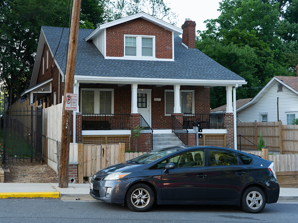 A two-story brick house with steps leading up to a porch with white pillars and a front door.