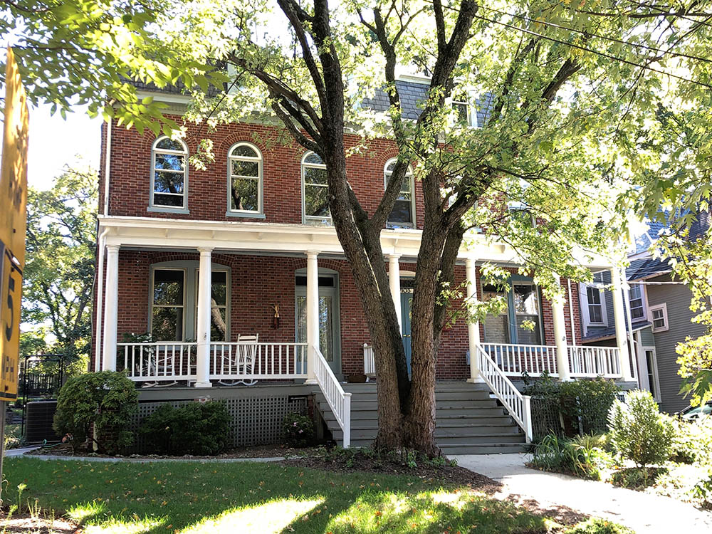 photo of a house that is a duplex in Takoma Park, MD. There is a tree in the front yard and there are two doors on the structure showing that this is a duplex