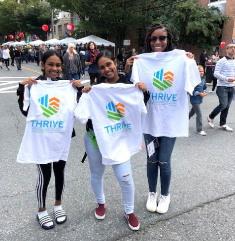 Woman and two girls holding up Thrive t-shirts at Taste of Bethesda