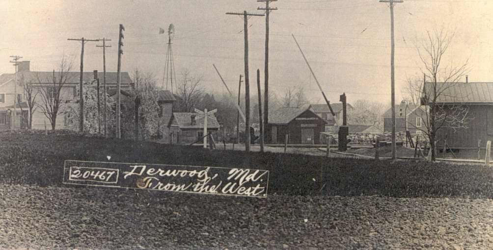 monochrome historic photo: "Derwood, MD from the west." Railroad crossing and buildings.