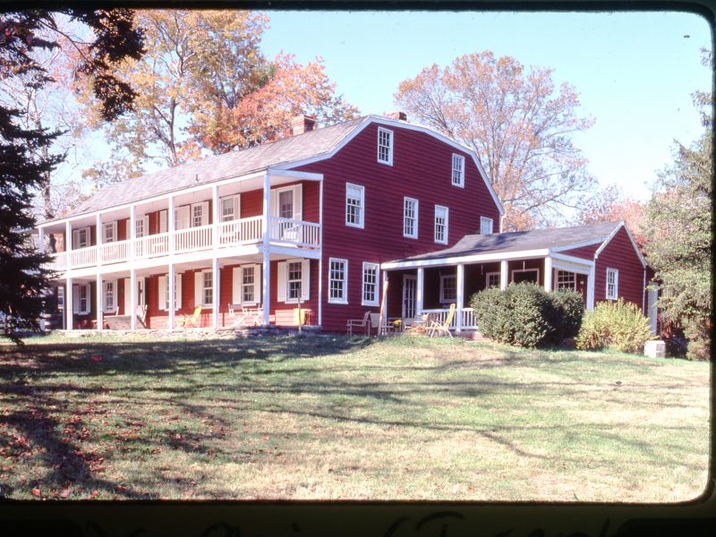 A red, gambrel-roofed farmhouse with white trim sits on a slight hill.