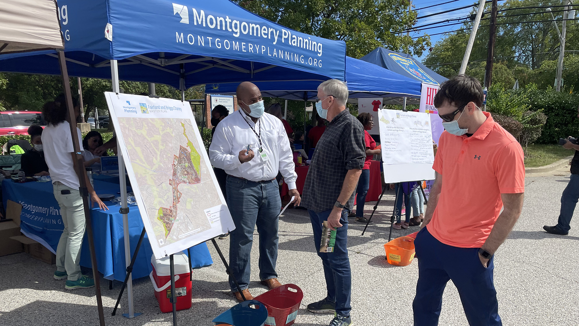 Staff speaks with community members standing by a map in front of a Montgomery Planning blue tent