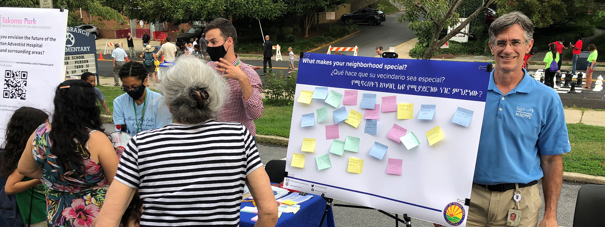 The image shows a man standing behind a sign at Takoma Park's National Night Out event that says 