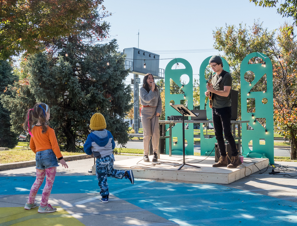 musical duo performs on outdoor stage while two children dance