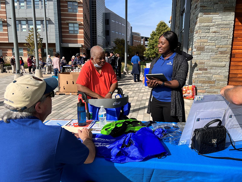 Montgomery Planning staff in blue shirts talk with a community member at an outdoor event
