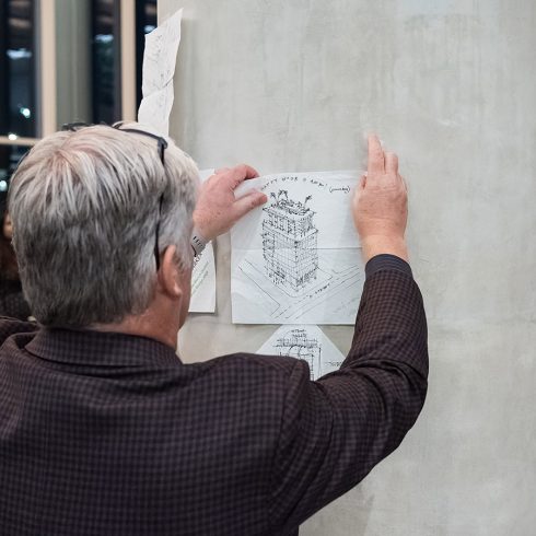 man tapes napkin with building sketch on pillar
