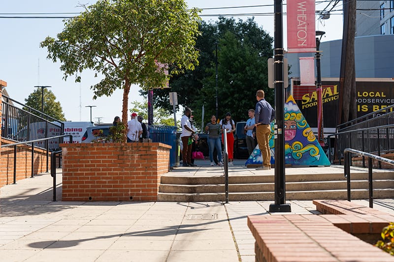 Group standing next to a pyramid-shaped painted art installation on sidewalk