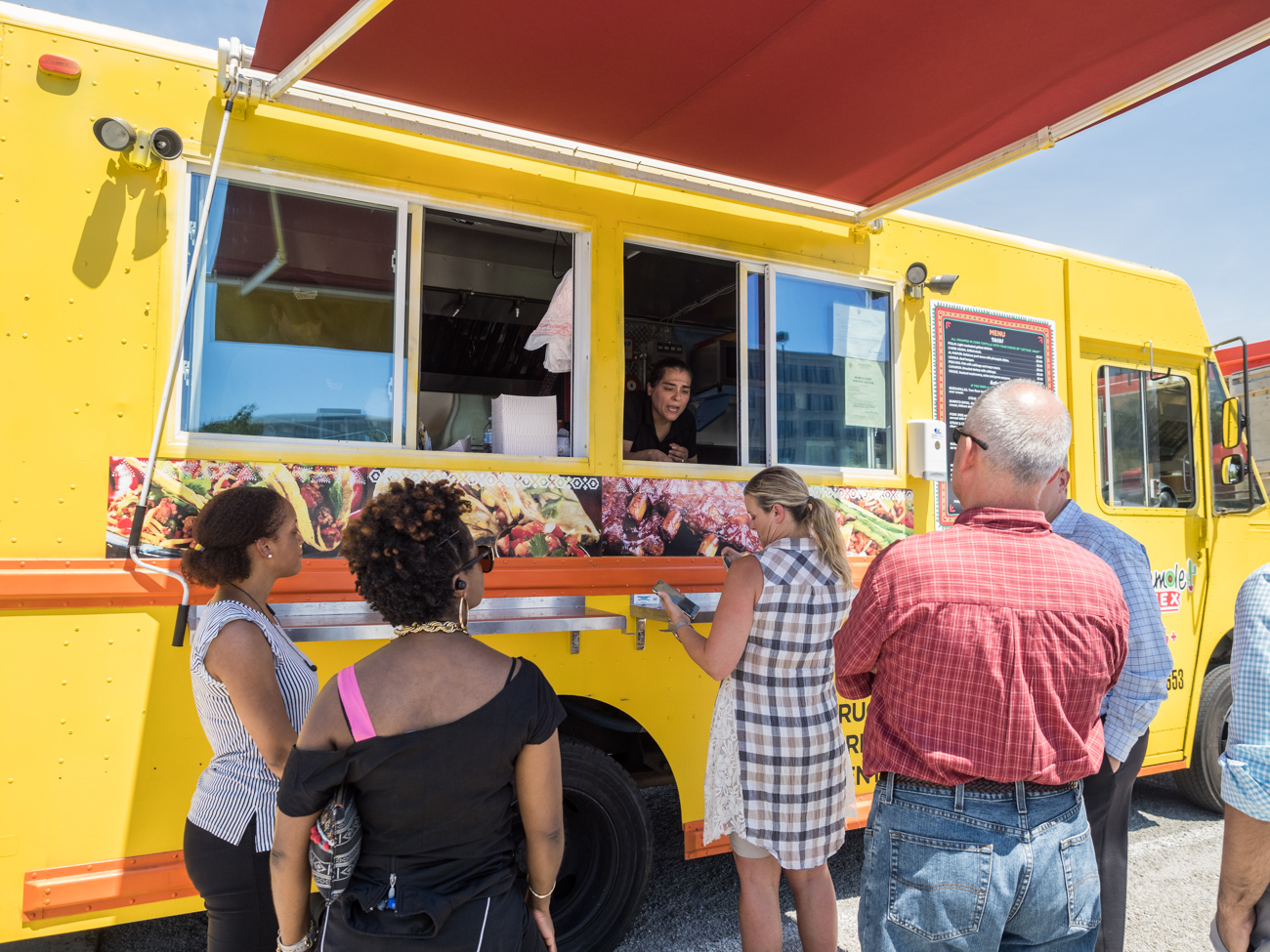 People standing in line at a bright yellow food truck while a vendor takes orders through the window.