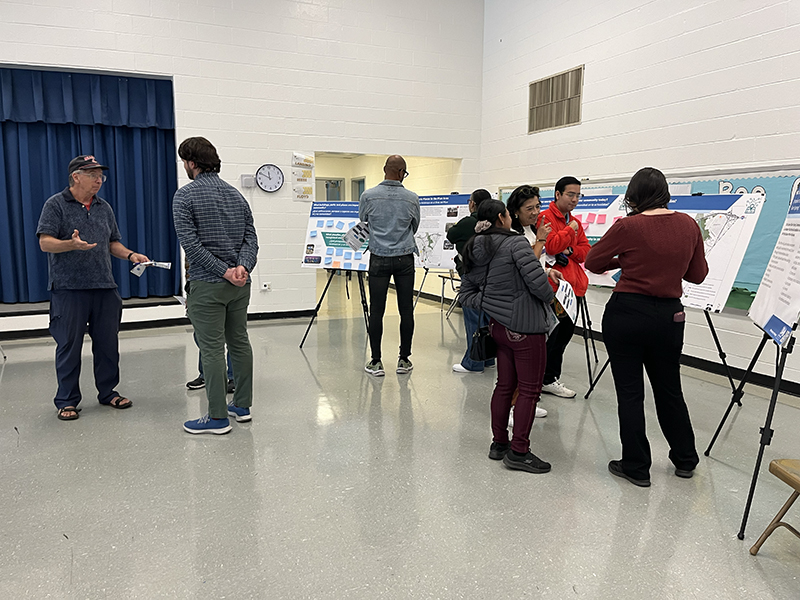 People engaging in discussions and viewing informational posters at an indoor event with white walls and a blue curtain.