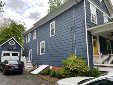 A side view onto a two-story blue house with a small garage visible alongside it.