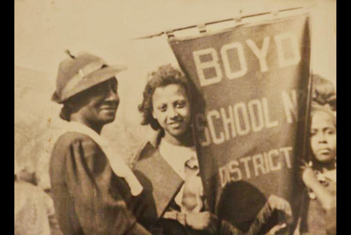 Two women and a young girl stand together holding a banner that reads "BOYD SCHOOL N DISTRICT" in a sepia-toned historic photograph.