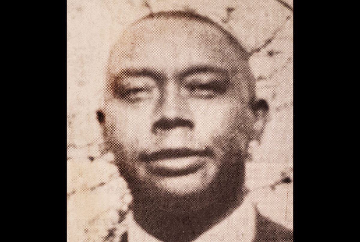 Black-and-white portrait of a man in a suit, facing forward with a neutral expression. The background appears textured or mottled.