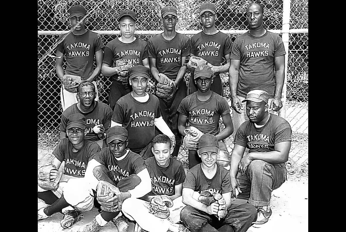 Black and white photo of a youth baseball team, "Takoma Hawks," posing in uniforms and gloves in front of a chain-link fence.