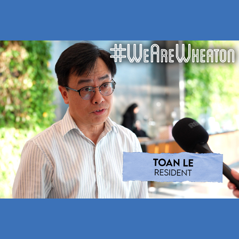 A man in glasses and a striped shirt is interviewed indoors. On-screen text reads "#WeAreWheaton" and "Toan Le, Resident.