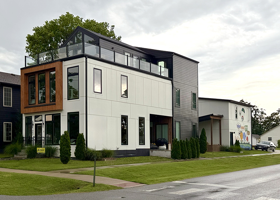 Modern two-story house with large windows, wood accents, and a rooftop patio, set on a green lawn with a sidewalk. A mural decorates a neighboring building, reflecting the vibrant community highlighted by Montgomery Planning.