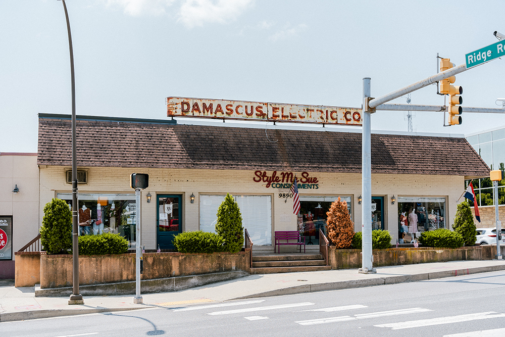 A single-story building with a faded "Damascus Electric Co." sign and a "Style Me Sue Consignments" storefront, located at a street corner with traffic lights.